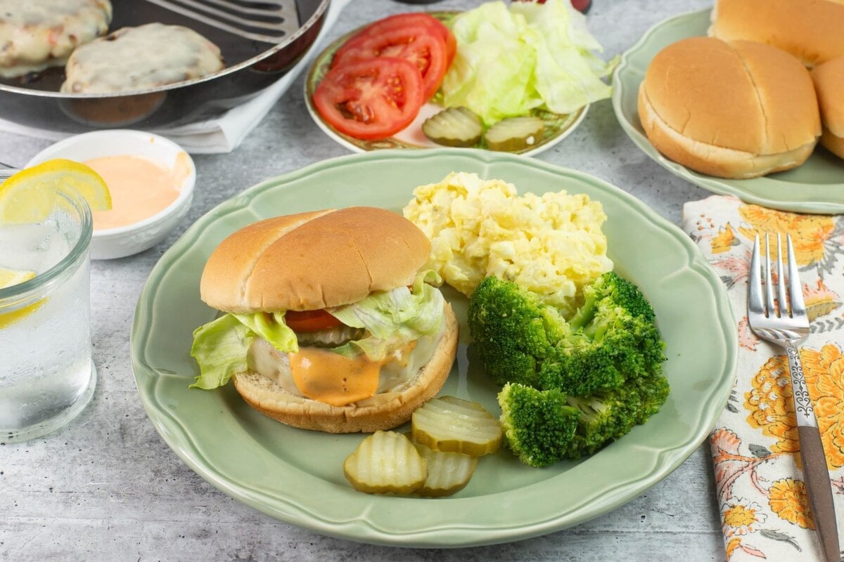 Homemade chicken burger meal served with sides and condiments plated on a dinner table.
