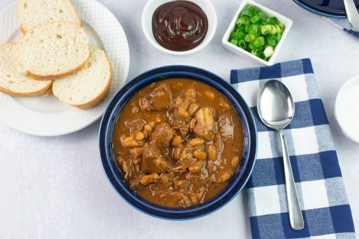 Ungarnished bowl of bbq shredded pork chili with bread and garnishes.