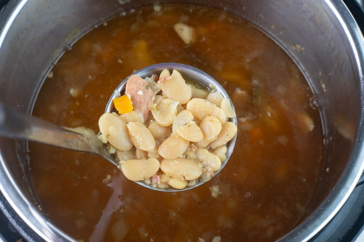 Ladle filled with cooked beans lifted out of the pot.