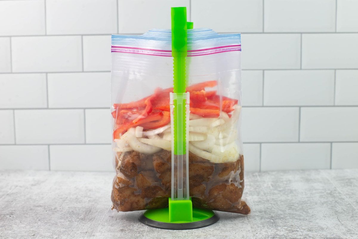 Standing plastic bag with layered seadoned chicken, sliced onions and sliced red bell pepper pieces.