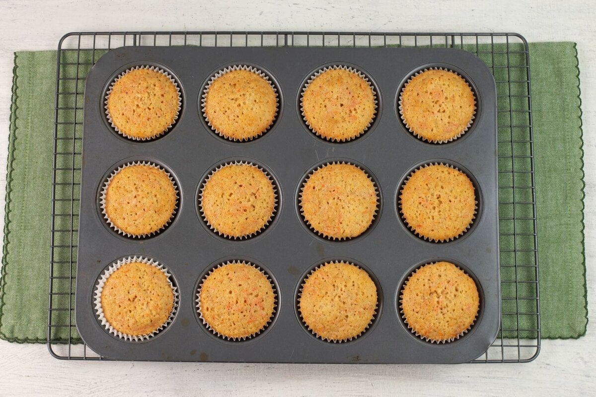 The baked cakes still in the cupcake pan cooling on a wire rack.