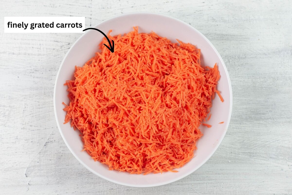 White bowl filled with finely grated carrots.