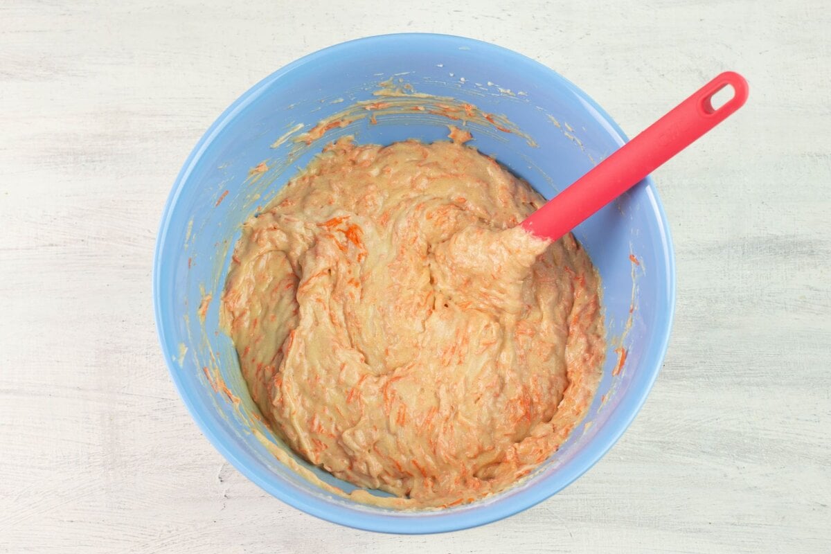Combining the grated carrots into the batter in a mixing bowl.
