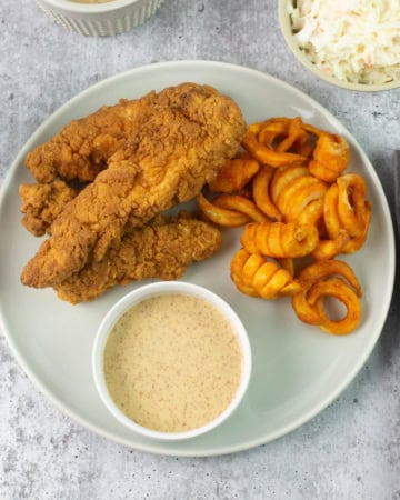 Bowl of honey mustard dipping sauce on plate with tenders and fries.