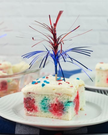Red White and Blue Poke Cake cut into a square, decorated patriotic on a dessert plate.