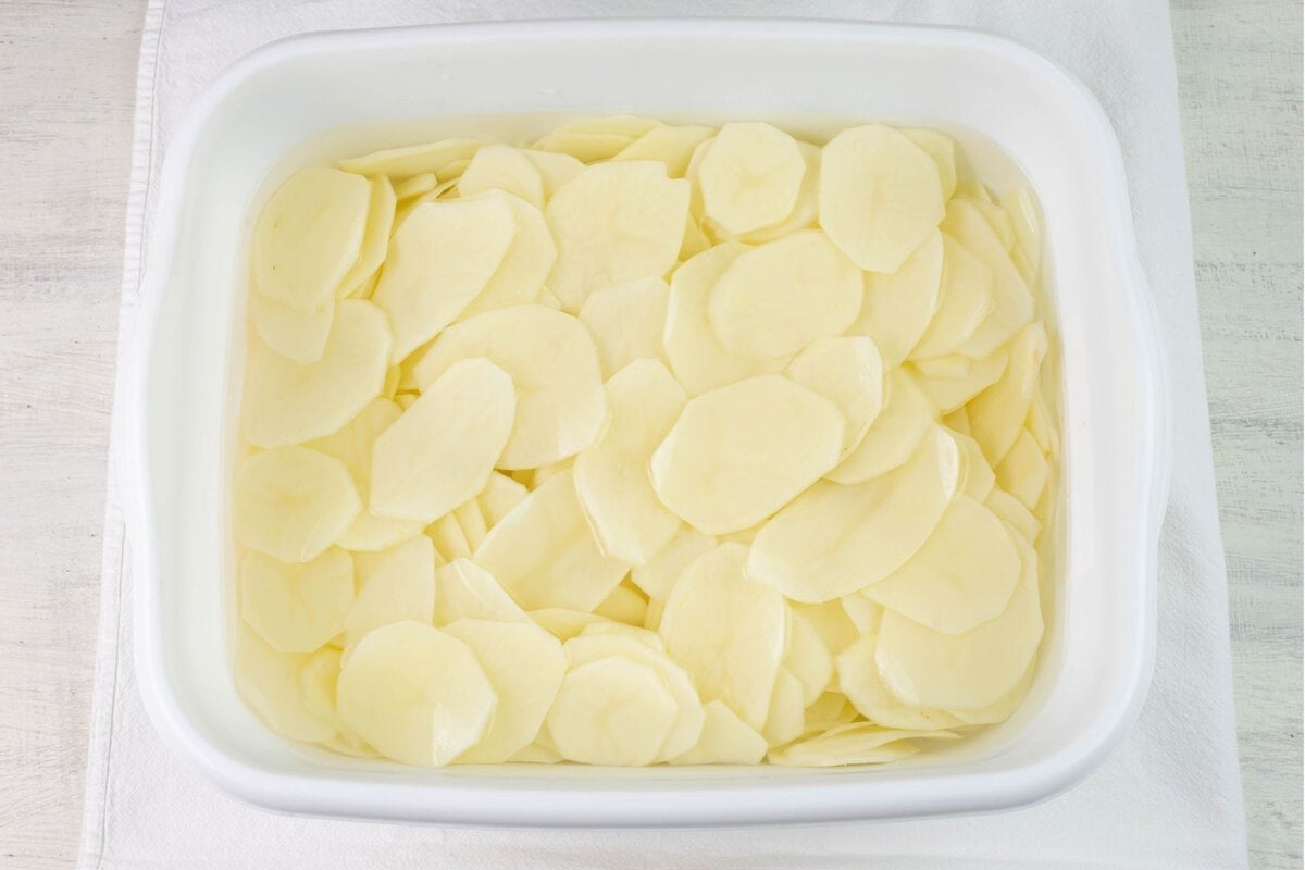 A plastic dishpan filled with washed, peeled, and sliced potatoes.