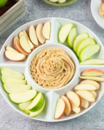 Peanut Butter Dip in the center of sliced apples in a round serving tray.